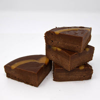 Stack of chocolate fudge pieces topped with caramel on a white background