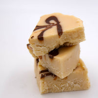 Stack of creamy fudge pieces with chocolate drizzle on a white background